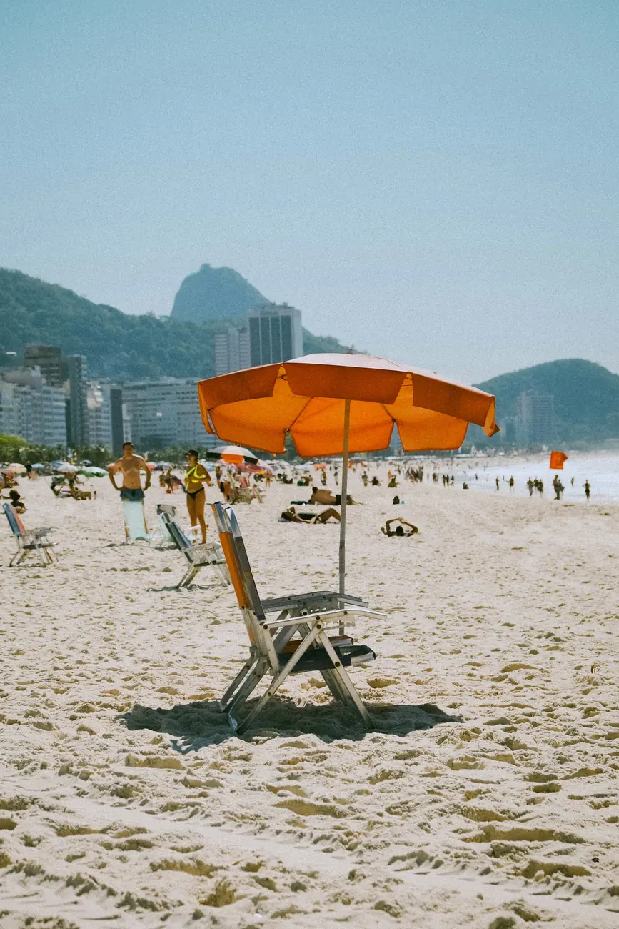 Guarda-sol laranja e cadeira na areia